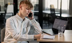 Młody mężczyzna rozmawia przez telefon, notując coś w zeszycie. Obok laptop i szklanka wody. Czy to numer 8012 co to za numer?