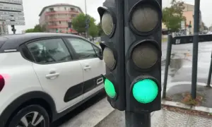 Un feu de circulation vert est allumé, indiquant que la circulation peut passer. Le gyrophare vert signification est la permission de continuer. Une voiture blanche est garée à proximité.