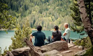 Tres personas disfrutan de las vistas del lago y el bosque, un descanso perfecto en las rutas Vall de Boí.