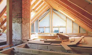 Interior de un altillo de madera en construcción, con vigas de madera, chimenea de ladrillo y materiales de construcción esparcidos.
