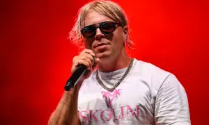Artysta Skolim w okularach i białej koszulce z napisem "SKOLIM" na czerwonym tle. Zastanawiasz się, ile Skolim bierze za koncert?
