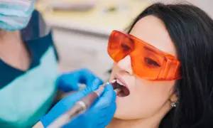 Pacjentka w okularach ochronnych przechodzi zabieg znieczulenia komputerowego zęba. Dentysta w rękawiczkach używa nowoczesnego urządzenia.