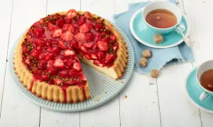 Ein schneller Erdbeerkuchen mit Paradiescreme, belegt mit frischen Erdbeeren und Pistazien. Dazu eine Tasse Tee.