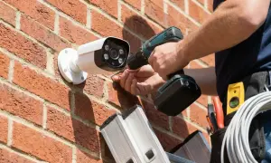 Installation d'une caméra de surveillance. Le **cctv signification** est la sécurité. Un technicien utilise une perceuse pour fixer la caméra sur un mur de briques.