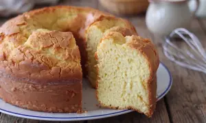 Il ciambellone della nonna, soffice e dorato, pronto per essere gustato. Sullo sfondo, uova e latte, ingredienti essenziali.