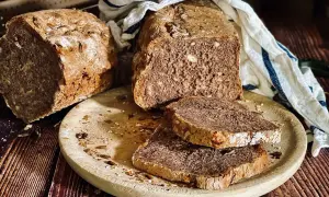 Frisch gebackenes Dinkelbrot mit Körnern und Nüssen, auf einem Holzbrett mit zwei Scheiben.