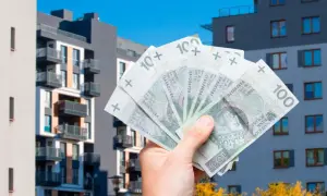 Dłoń trzyma polskie banknoty 100 zł na tle nowoczesnych bloków mieszkalnych. To symbol ulgi mieszkaniowej i możliwości zakupu własnego lokum.