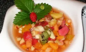 Salade de fruits maison colorée, garnie d'une fraise et de feuilles de fraisier.