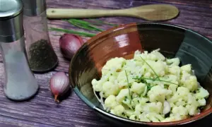 Frischer blumenkohl salat mit Schalotten und Schnittlauch in einer rustikalen Schüssel, daneben Salz- und Pfefferstreuer.