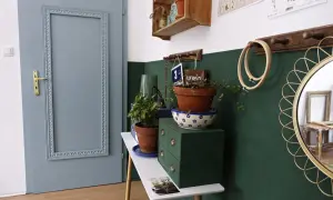 Szare drzwi pokojowe z ozdobną ramą, obok zielona komoda z roślinami. Zastanawiasz się, ile kosztuje malowanie drzwi pokojowych?