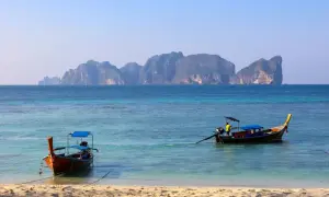 Dwa tradycyjne tajskie łodzie dryfują na turkusowej wodzie. W tle widać skaliste wyspy. Idealne miejsce na wakacje w Tajlandii, Phuket.