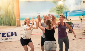 Fyra glada kollegor ger varandra high-fives på en sandstrand. Perfekta tips på aktiviteter med kollegor för teambuilding!