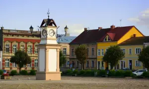 Rynek w **Lwówek Wlkp.** z zegarową wieżą po lewej i kolorowymi kamienicami w tle.