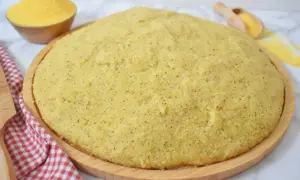 Gotowa, puszysta polenta na drewnianej desce, obok miseczka z mąką kukurydzianą.