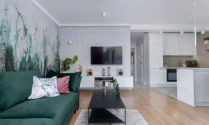 Nowoczesny pokój z telewizorem, zieloną kanapą i designerską tapetą. W tle widać kuchnię.
