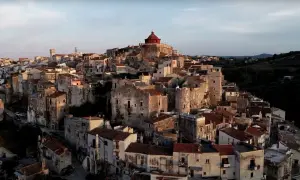 Antico borgo di Vico del Gargano, con case in pietra e tetti rossi che si aggrappano alla collina, dominato da una chiesa con cupola rossa.
