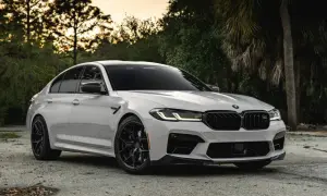 Białe BMW M5 G30 z czarnymi felgami i detalami, zaparkowane na tle drzew i zachodzącego słońca.