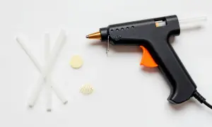 Czarny pistolet do kleju na gorąco z pomarańczowym spustem i kilkoma pałeczkami kleju obok. Dowiedz się, jak włożyć klej do pistoletu.