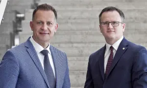 Dwóch mężczyzn w garniturach stoi na tle schodów.