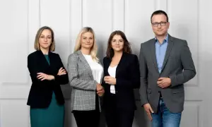 Cztery osoby w strojach biznesowych stoją obok siebie na jasnym tle.