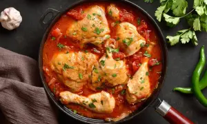 Pyszny kurczak w sosie pomidorowym, duszony z cebulą i posypany natką pietruszki. Obok czosnek, pomidory i papryczki chili.