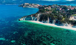 Arcipelago Toscano: una costa con scogliere bianche, spiaggia dorata e mare cristallino, con un borgo storico in lontananza. Un gioiello tra le isole visitabili.