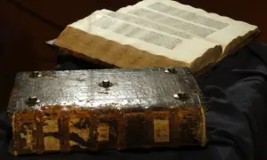 Stary, zniszczony księgozbiór w stylu biblijnym, z metalowymi okuciami i otwartą księgą pełną tekstu.