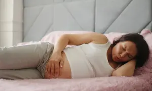 Kobieta w 6. tygodniu ciąży leży na boku, trzymając się za brzuch. Wygląda na to, że odczuwa ból brzucha.