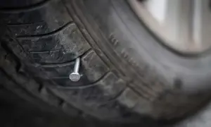 Un clou rouillé est planté dans la bande de roulement d'un pneu usé, prêt à causer une crevaison.
