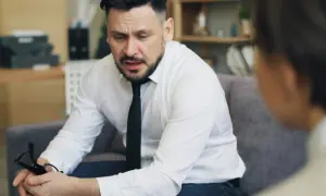 Mężczyzna w białej koszuli i krawacie, trzymający okulary, zastanawia się, jak inteligentnie zakończyć rozmowę.