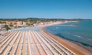 Fano mare: file ordinate di ombrelloni bianchi e colorati sulla sabbia dorata, con il mare azzurro e la costa sullo sfondo.