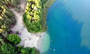 Plaża nad jeziorem tętni życiem. Ludzie odpoczywają na piasku, kąpią się w krystalicznie czystej wodzie, ciesząc się letnim dniem.
