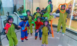 Niños con cascos y trajes verdes disfrutan de experiencias únicas, algunos con globos de colores, en un túnel de viento.