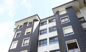 Modernas fachadas con cerámica gris y blanca, con ventanas de diferentes tamaños y persianas enrollables, bajo un cielo azul con nubes.