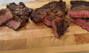 Tre saftiga steak minute-biffar, perfekt stekta med rosa kärna, ligger på en träskärbräda.