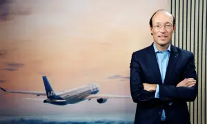 SAS VD, en man i kostym, står framför en bild av ett flygplan i solnedgången.