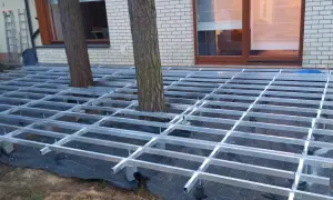 Trwa układanie deski kompozytowej na aluminiowym stelażu, który omija drzewa rosnące na tarasie.