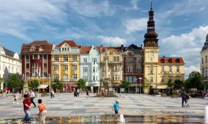 Kolorowy plac w Ostrawie z ludźmi i zabytkowymi budynkami w tle.