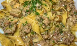 Pappardelle cremose con salsiccia e funghi, guarnite con prezzemolo fresco. Un piatto ricco e saporito.