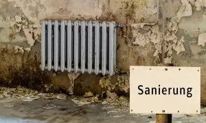 Altes Heizkörper, Wand bröckelt, ein Schild mit "Sanierung" weist auf den Zustand hin. Es ist offensichtlich, dass hier etwas leck und undicht ist.