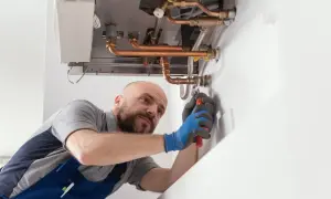Un tecnico con guanti blu lavora su una caldaia, cercando di capire perché la caldaia perde pressione ma non ci sono perdite visibili.