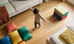 Kleines Kind balanciert auf roter-weißer Linie, ein tolles Beispiel für Koordinationsspiele für Kinder. Bunte Kissen und Bausteine laden zum Spielen ein.