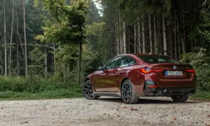 Ciemnoczerwone BMW Gran Coupé na szutrowej drodze w lesie.