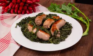 Salsiccia e friarielli, un piatto tradizionale napoletano, servito su un piatto bianco con peperoncini rossi sullo sfondo.