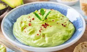 Cremige Avocado-Creme, garniert mit Minze, Sesam und Chiliflocken, serviert in einer blauen Schüssel.