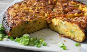 Pyszna tortilla de patatas, pokrojona na kawałki, z zieloną cebulką na talerzu.
