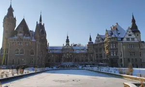 Zamek Moszna w zimowej scenerii, z zamarzniętym stawem i ośnieżonymi dachami. Bajkowa budowla prezentuje się majestatycznie.