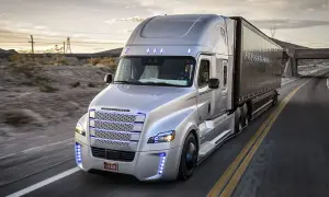 Un camion américain nez plat argenté roule sur une route déserte au coucher du soleil.