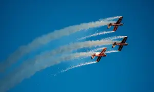 Trzy samoloty akrobacyjne w formacji, wypuszczające dym i iskry na błękitnym niebie. Niezapomniane wrażenia z kiedy air show w Radomiu.