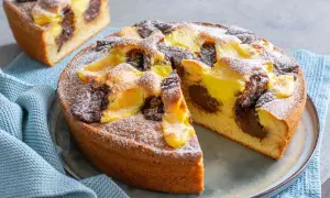 Torta nua con crema pasticcera e cacao, spolverata di zucchero a velo. Una fetta è già stata tagliata, rivelando il morbido interno.